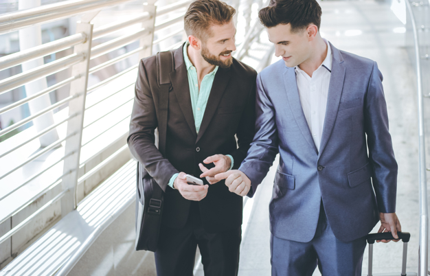 two-businessman-talking-and-walking-while-using-smartphone-at-sidewalk-of-modern-building_t20_XQr72X